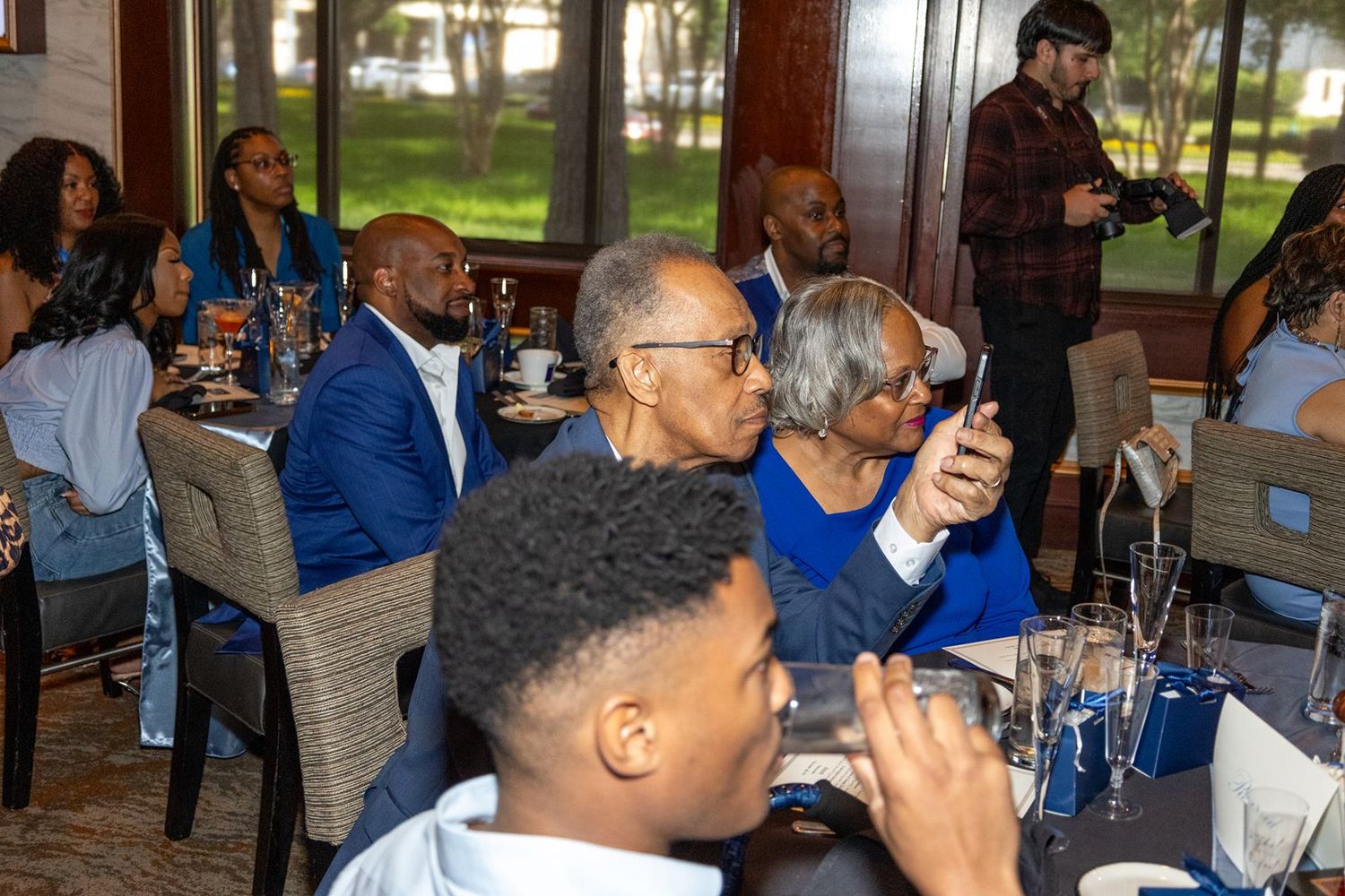 Guests gathered at an elegant dinner event, dressed in formal attire, socializing at decorated tables in a upscale venue.