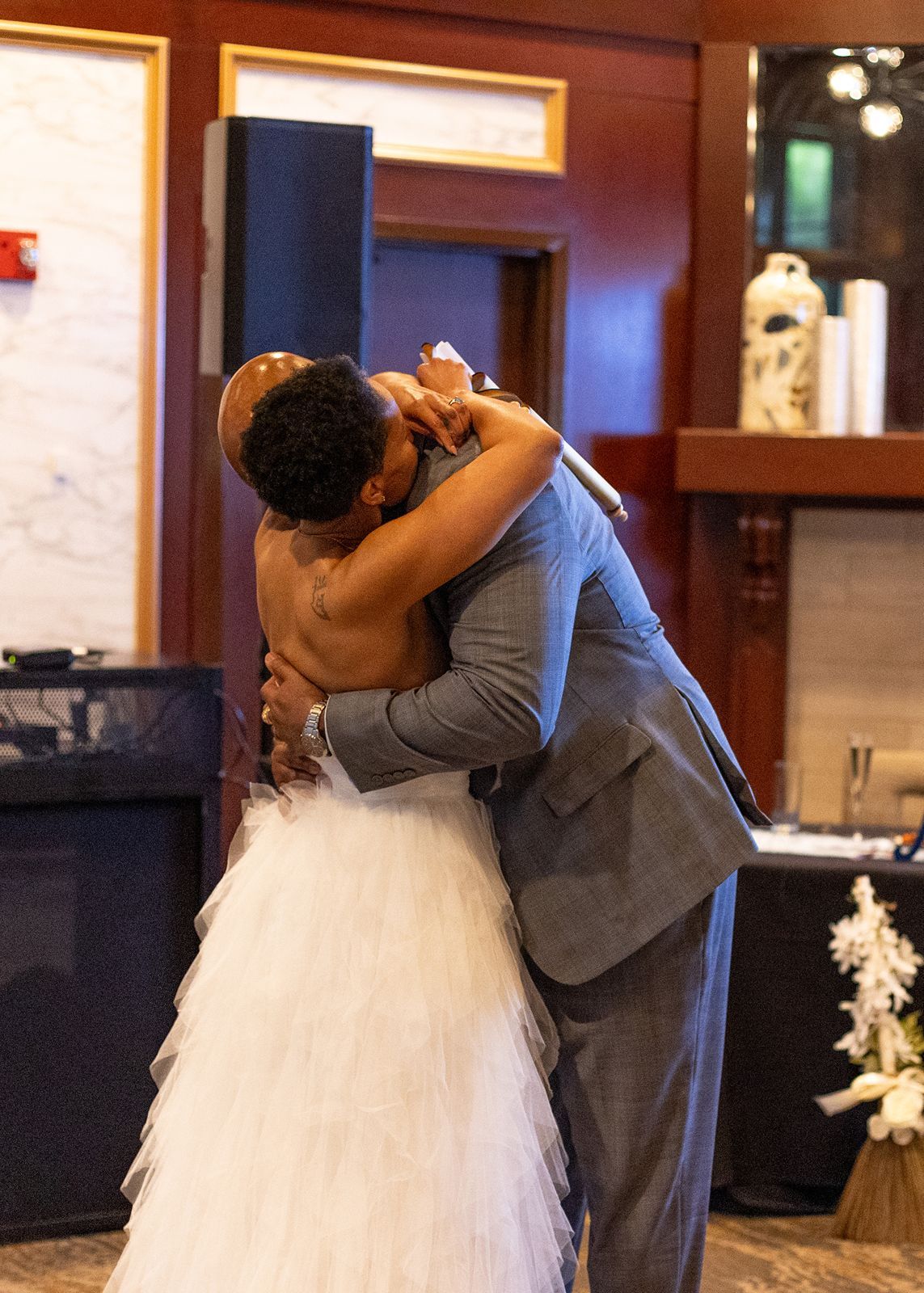 A bride in a white tulle gown and groom in a gray suit share an emotional first dance embrace at their wedding reception.