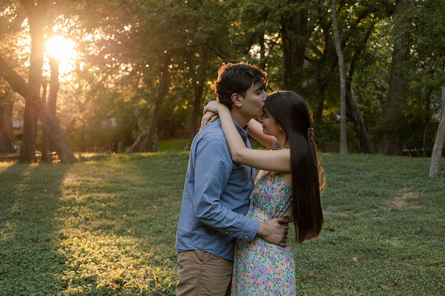 Romantic couple shares tender moments at sunset in a park setting during a golden hour photoshoot.