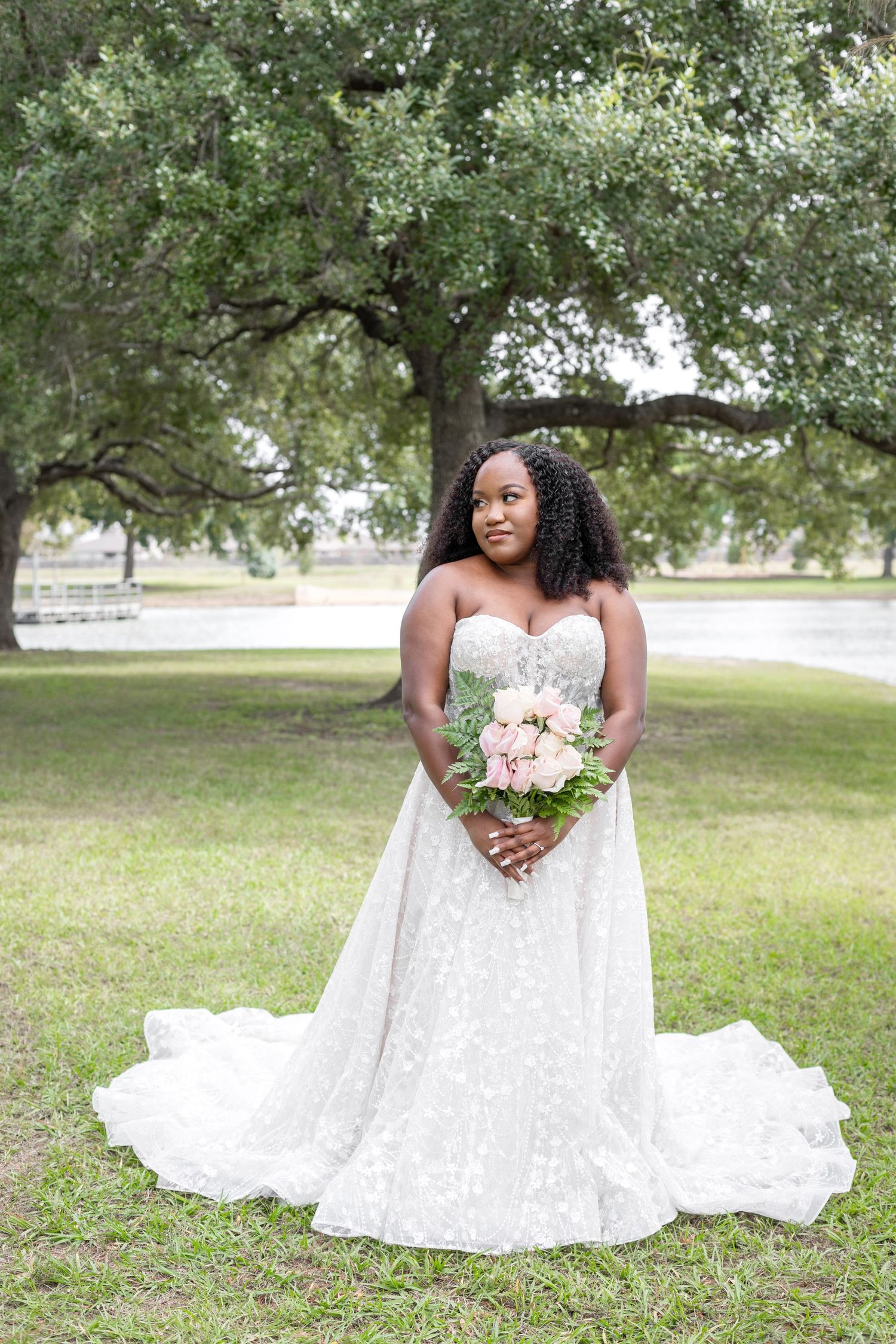 Bride in flowing white lace gown poses in outdoor garden setting.