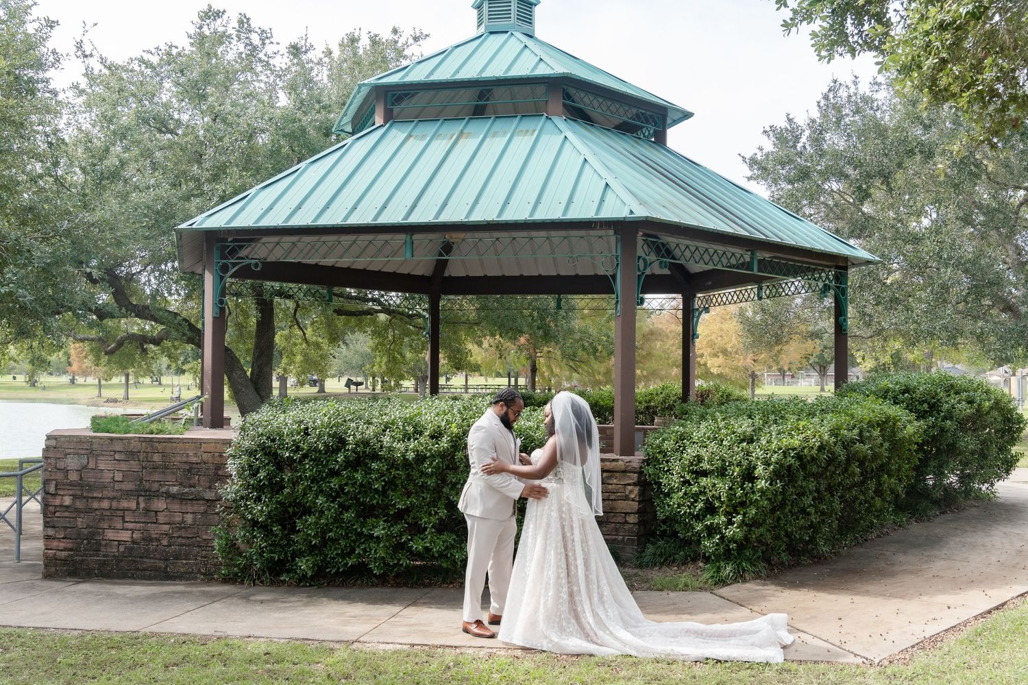 Outdoor wedding venue featuring a green-roofed gazebo surrounded by manicured hedges and trees.