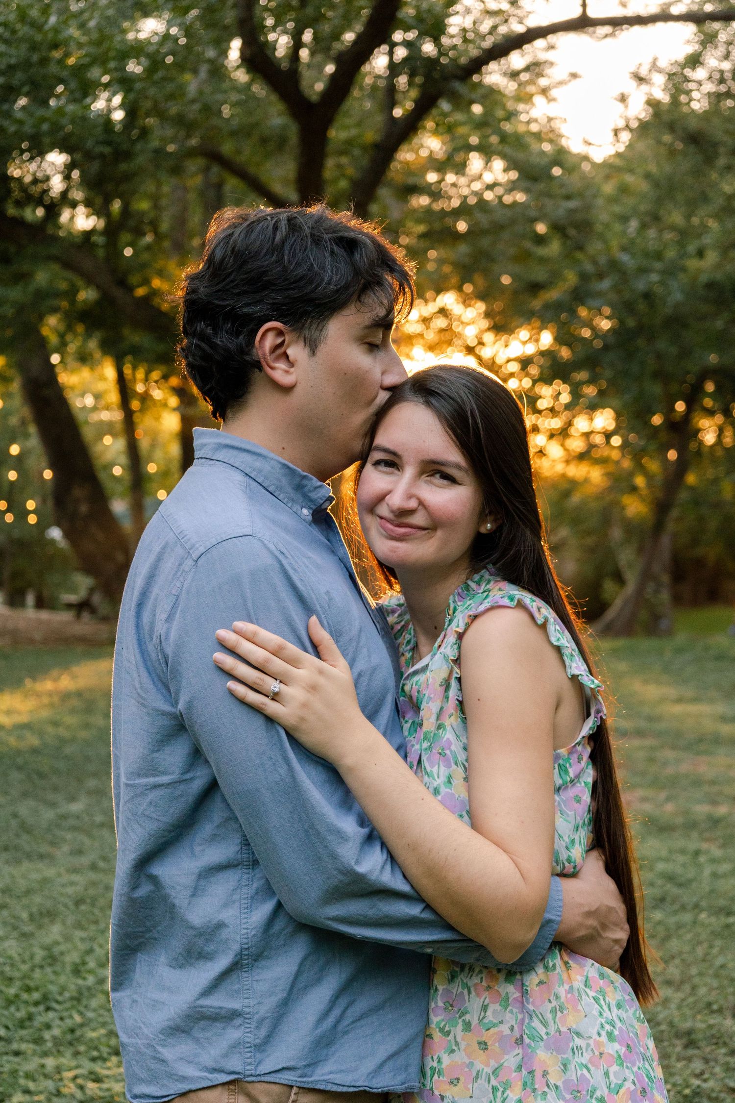 Romantic couple embracing in a golden sunset light under trees in a park.