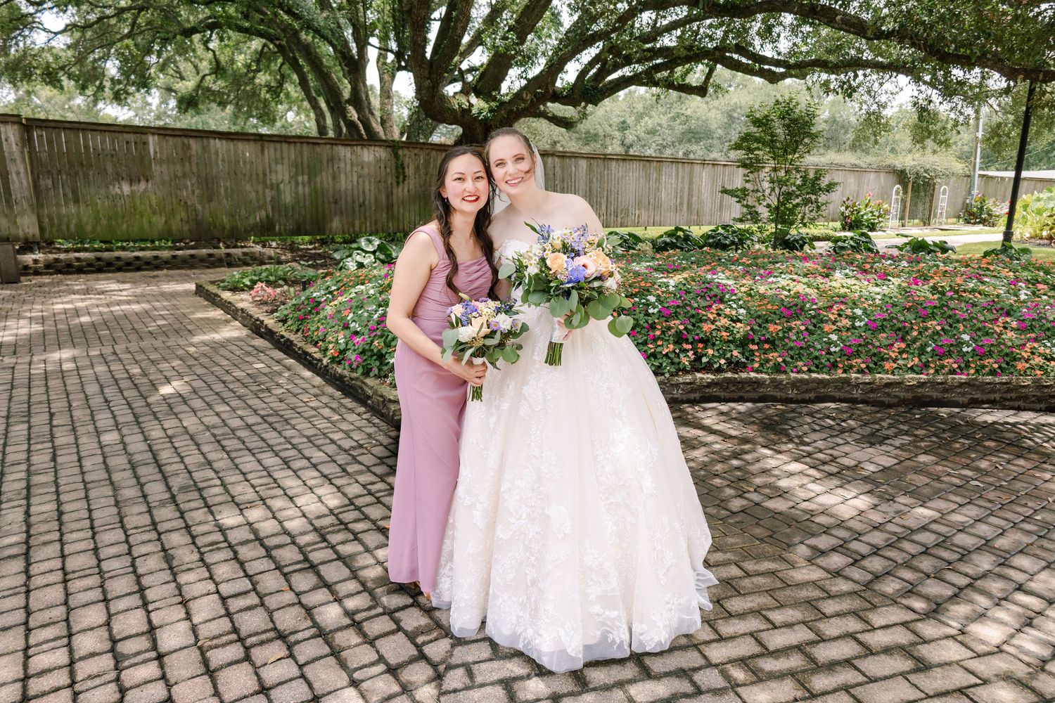 Wedding party poses for photos on brick pathway surrounded by blooming garden flowers.