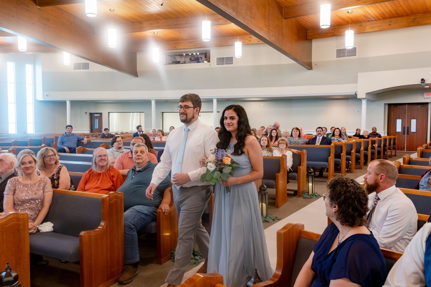 Church sanctuary with exposed wooden beams and pendant lighting during a wedding ceremony.