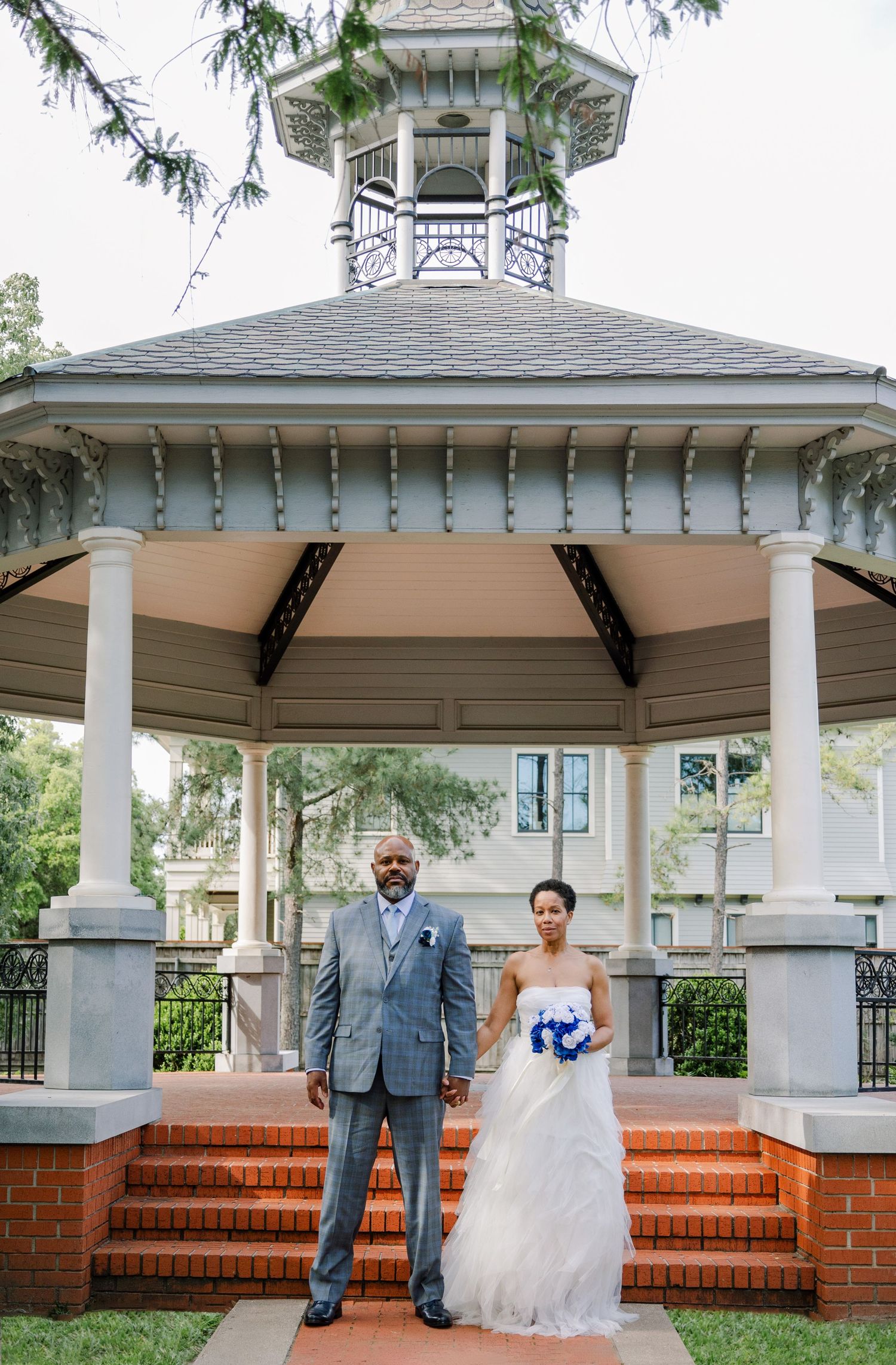 A wedding couple poses in front of a white gazebo with brick steps and columns at different angles.