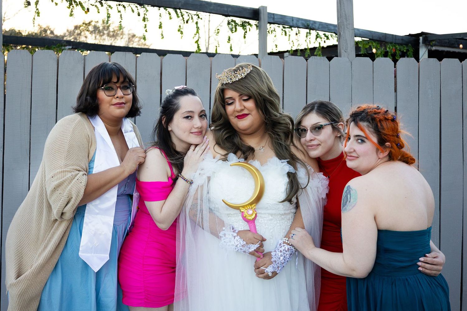 Five women posing together outdoors, one dressed as Sailor Moon in white costume with crown and wand.