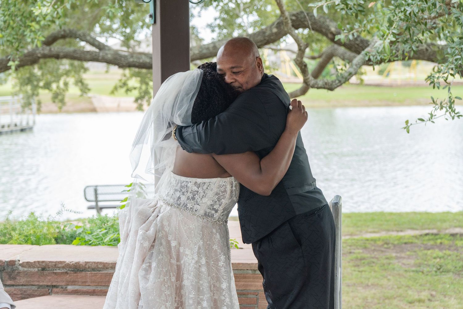 Wedding party members share embraces and candid moments under outdoor pavilion.