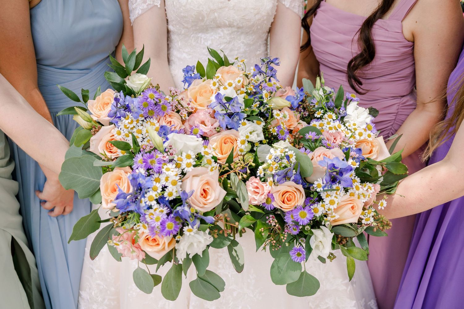 Close-up of wedding bouquets featuring peach roses, purple flowers, and eucalyptus greenery.