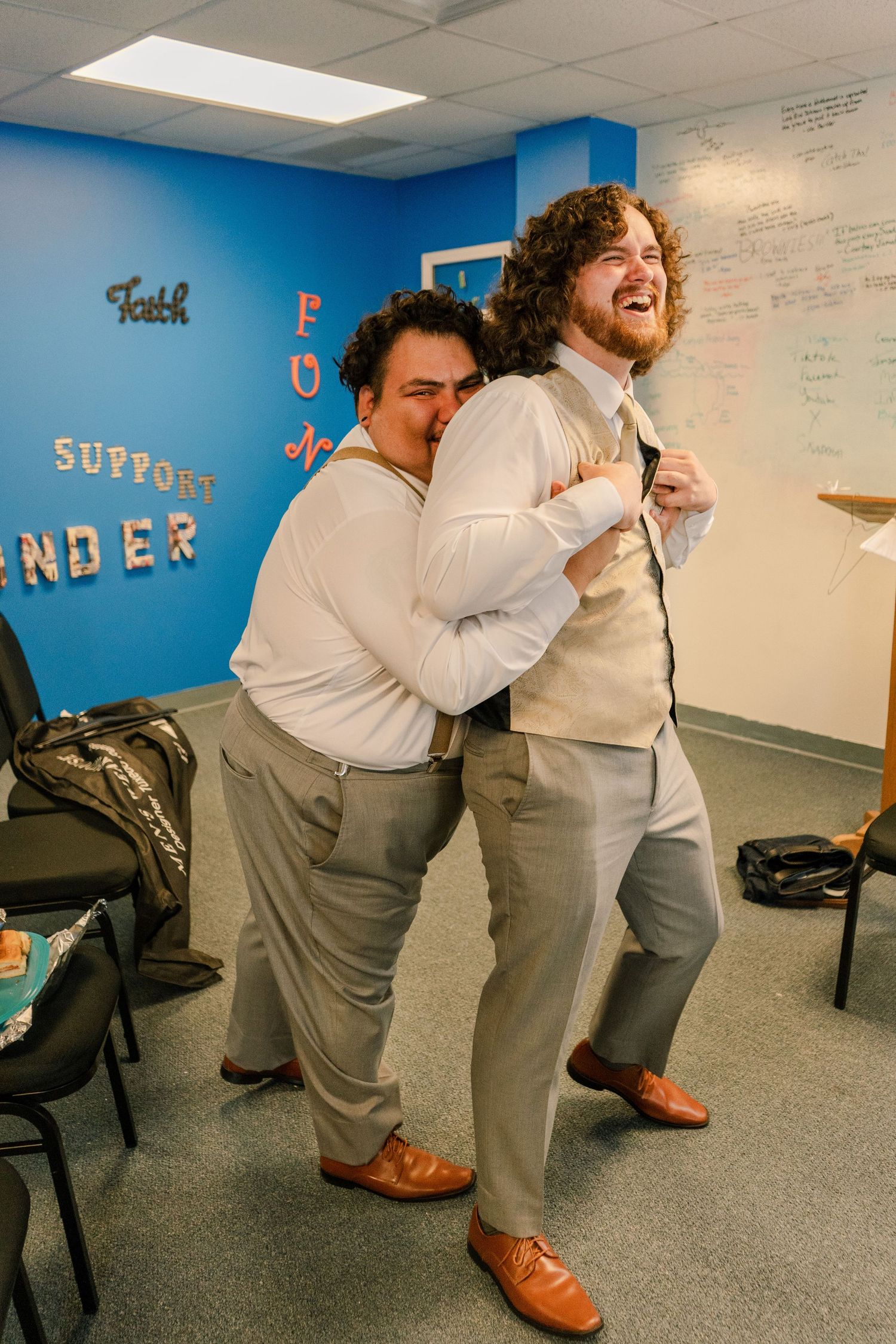 Wedding party members in formal attire sharing a lighthearted moment in a blue room.