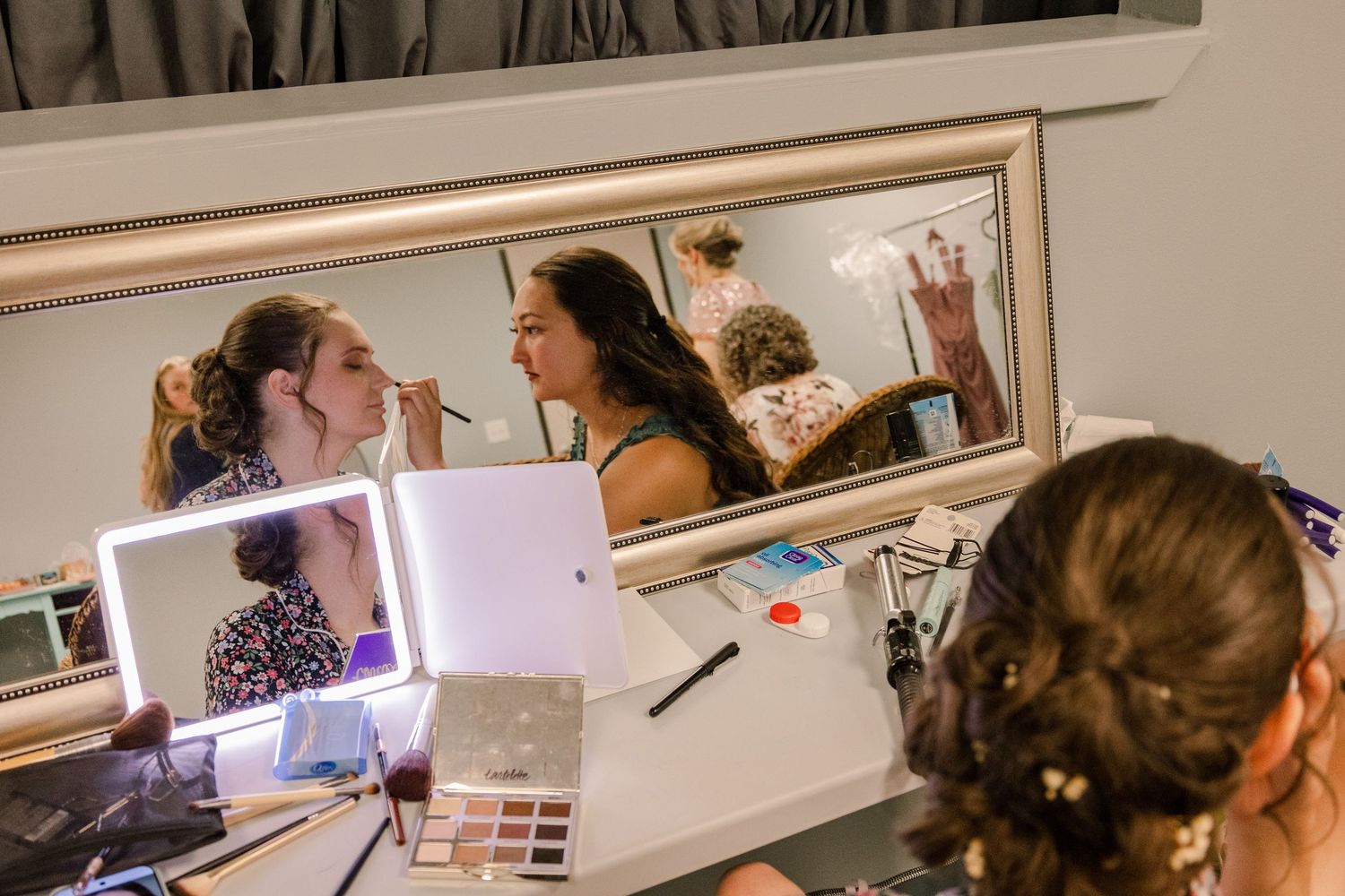 A group having fun getting ready in a wedding preparation room with mirrors and lighting.