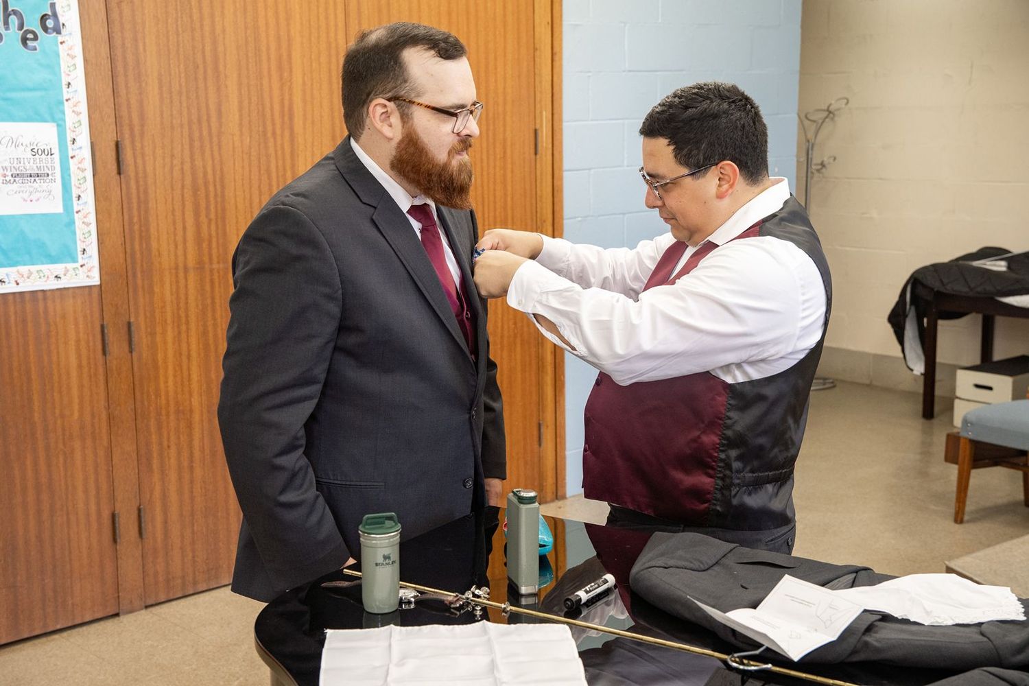 A man in a suit gets his tie adjusted by a colleague in a professional office setting.