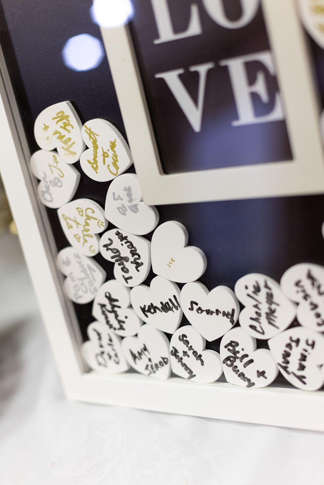 White shadow box frame with LOVE text filled with small heart-shaped guest book signatures at a wedding reception.