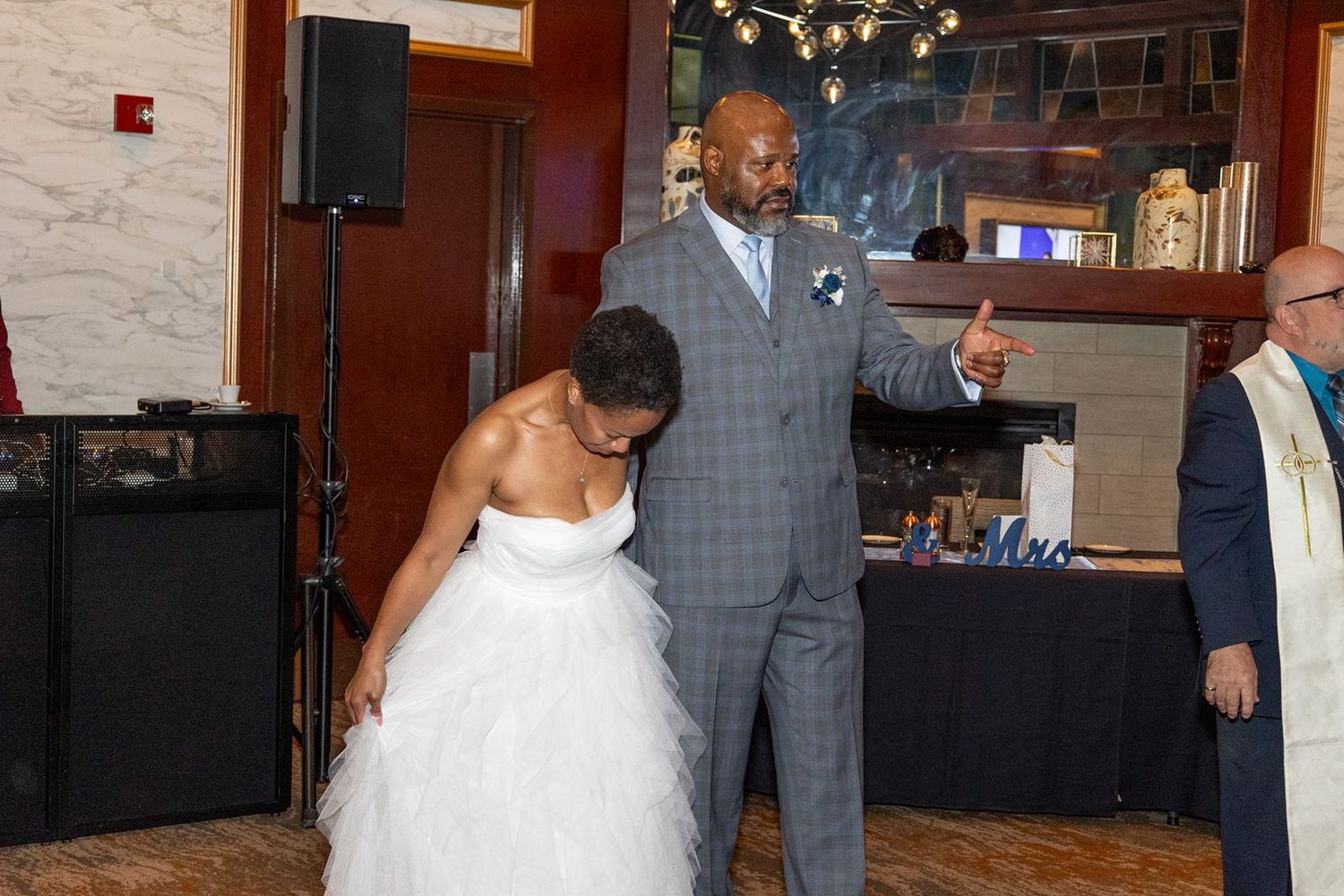 Bride in white gown and groom in gray suit share a joyful moment during their wedding reception indoors.