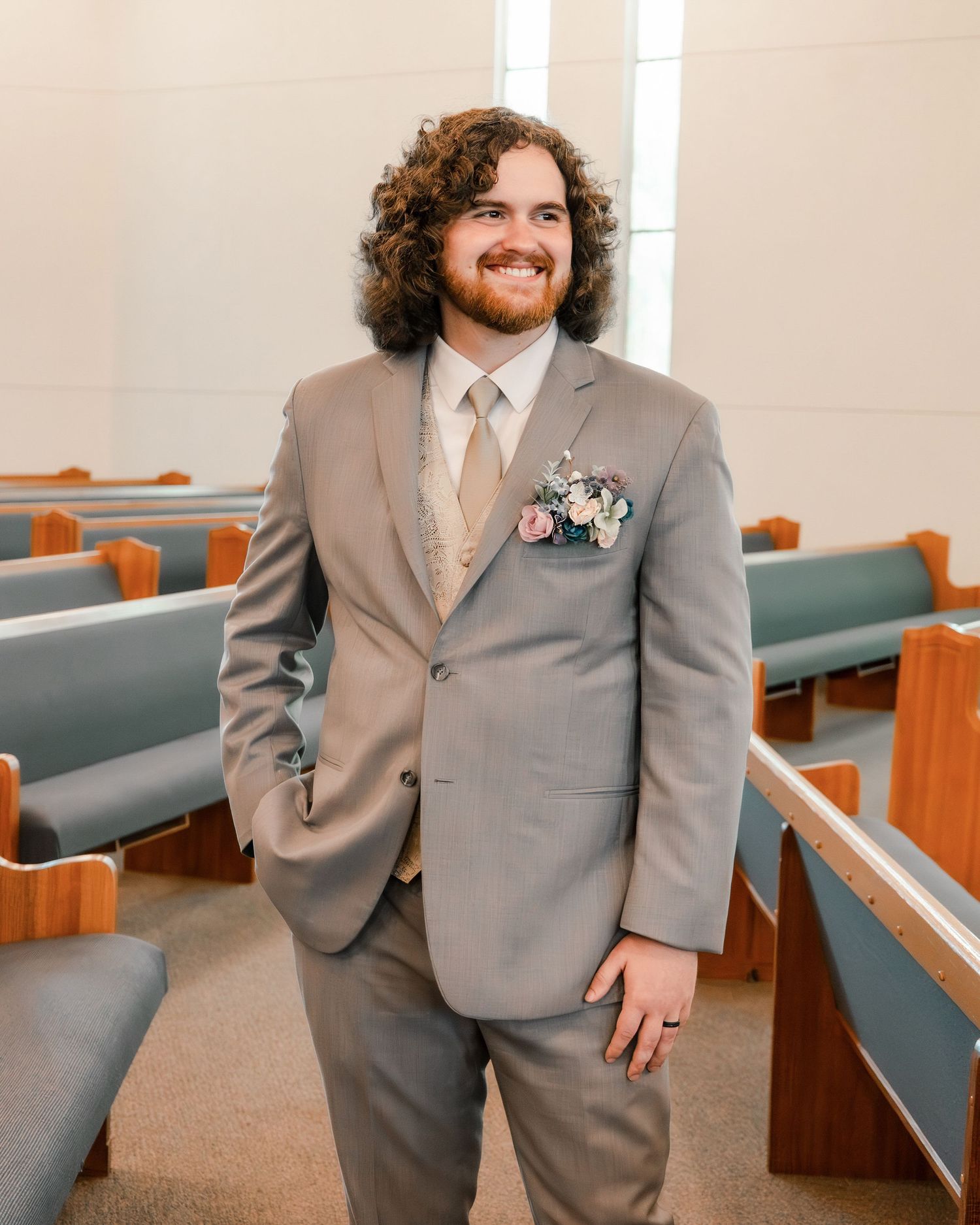 A formal portrait in a grey suit with boutonniere inside a church sanctuary.