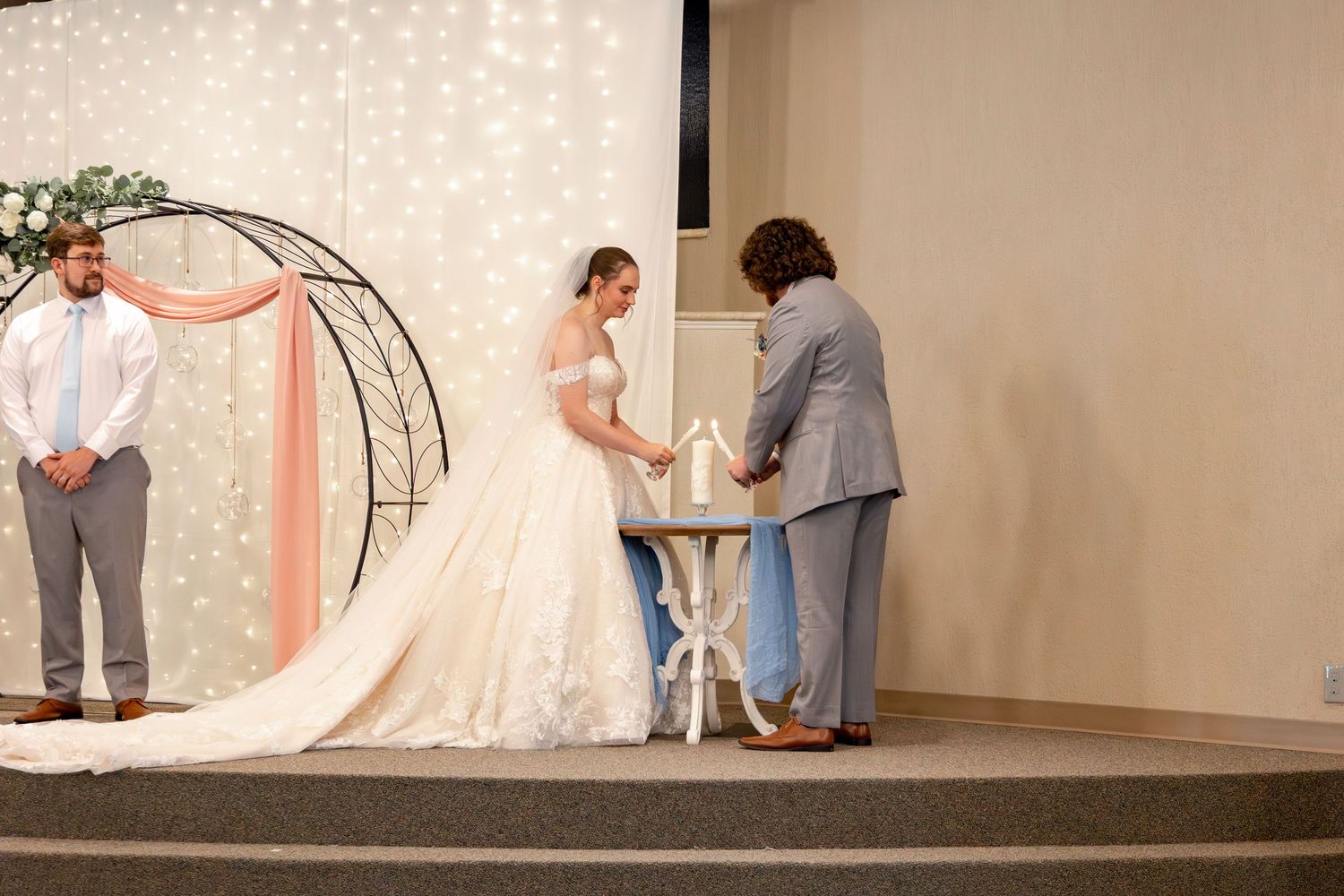 A wedding ceremony with an arch decorated with greenery and twinkling lights in the background.