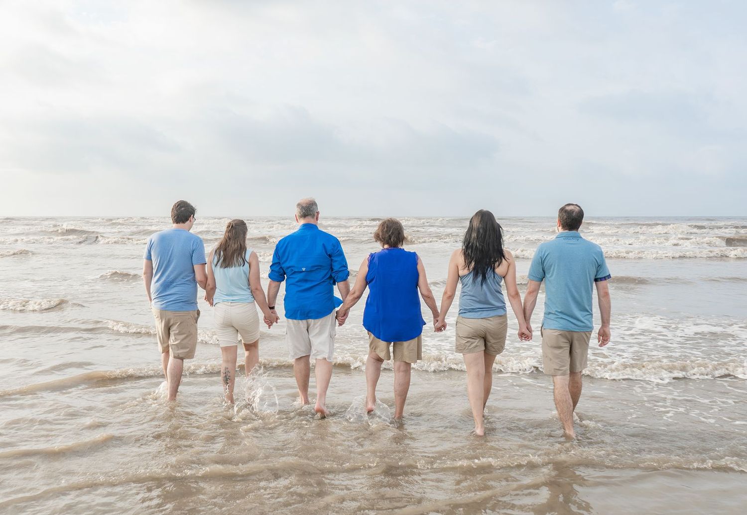 A group of people walking together along the beach shoreline wearing coordinated blue and white outfits.