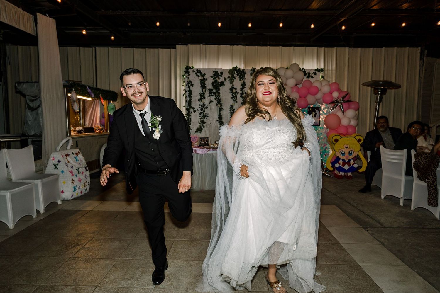 Bride and groom making grand entrance at wedding reception in decorated venue with floral backdrop.