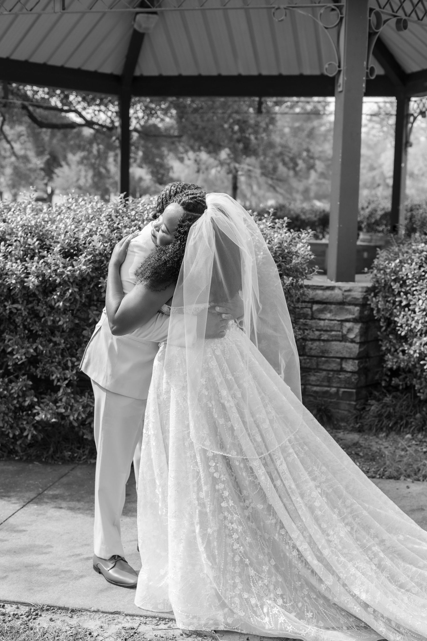A beautiful white lace wedding dress with a long flowing train is displayed under an outdoor gazebo.