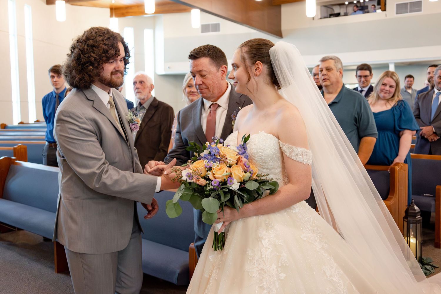 Wedding guests gather in a church sanctuary decorated with light backdrops.