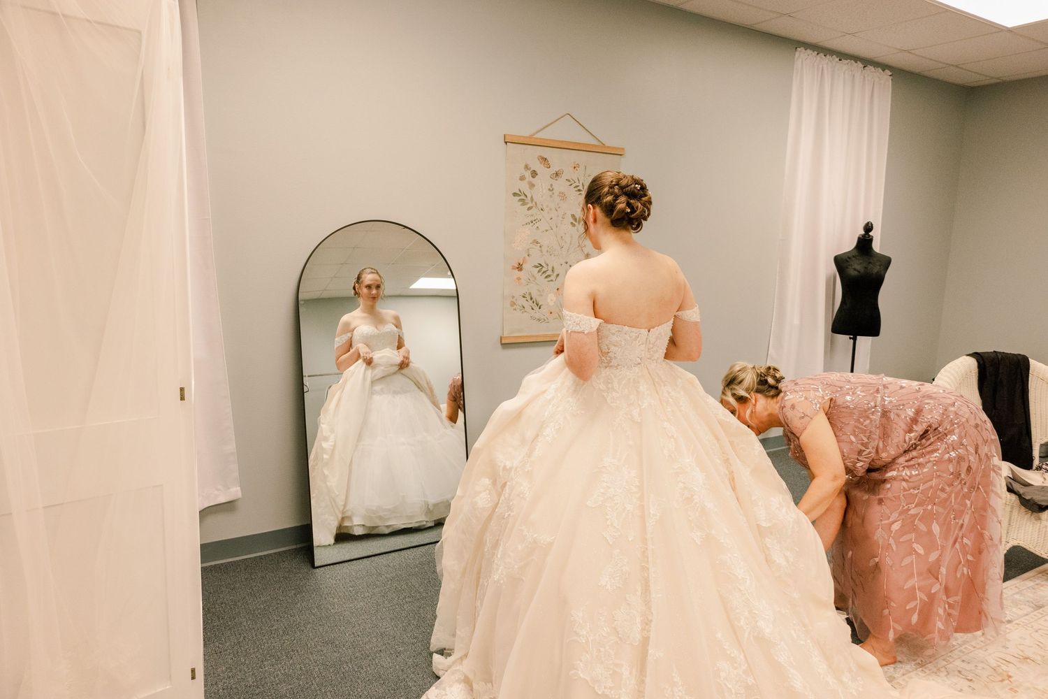 Wedding dress fitting session in bridal salon with mirror and black dress form.