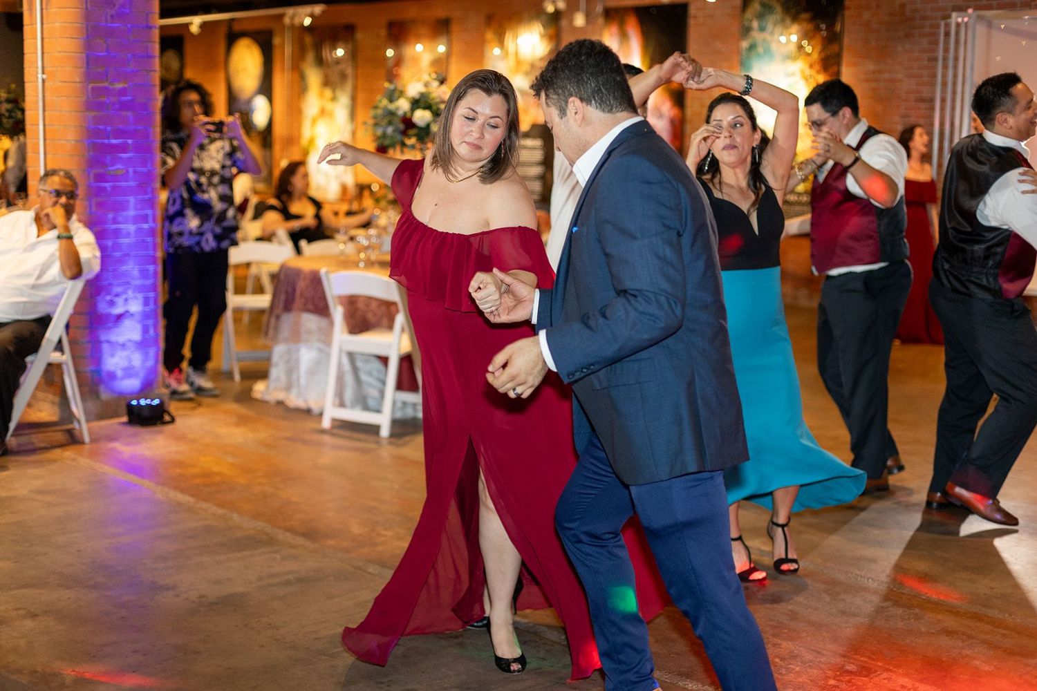 Woman in red gown dancing with partner at festive wedding reception celebration.