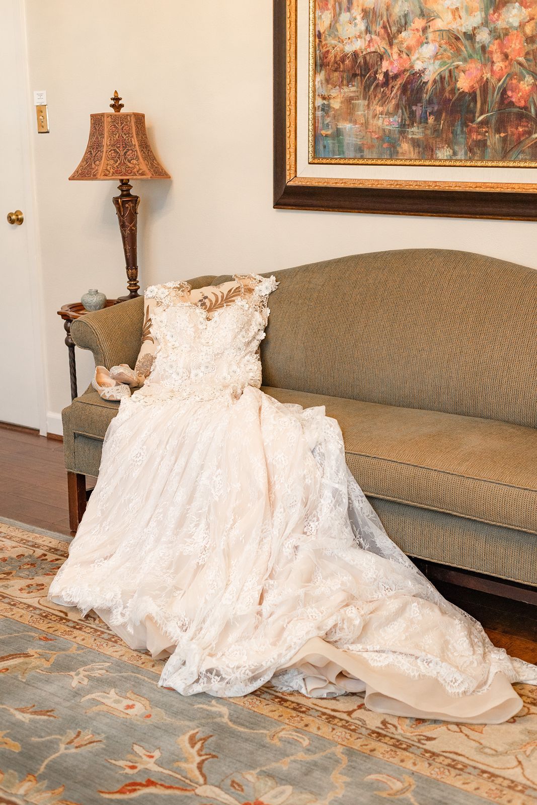 Elegant lace wedding gown draped over vintage green sofa in warmly lit room.