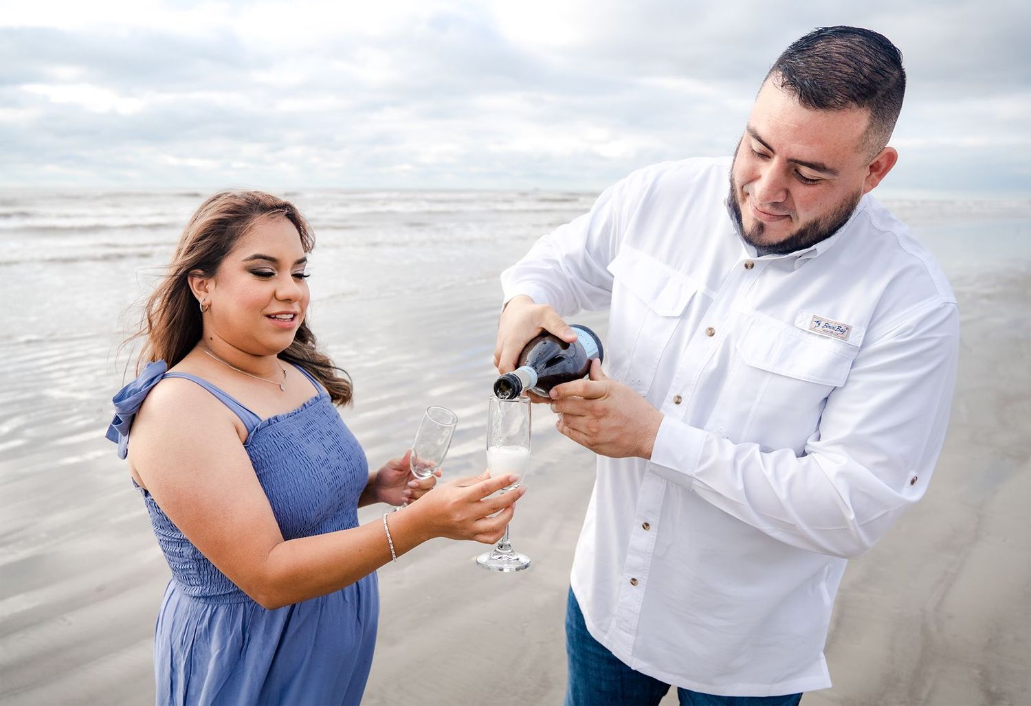 A couple shares a romantic moment on a cloudy beach while looking at their phones together.