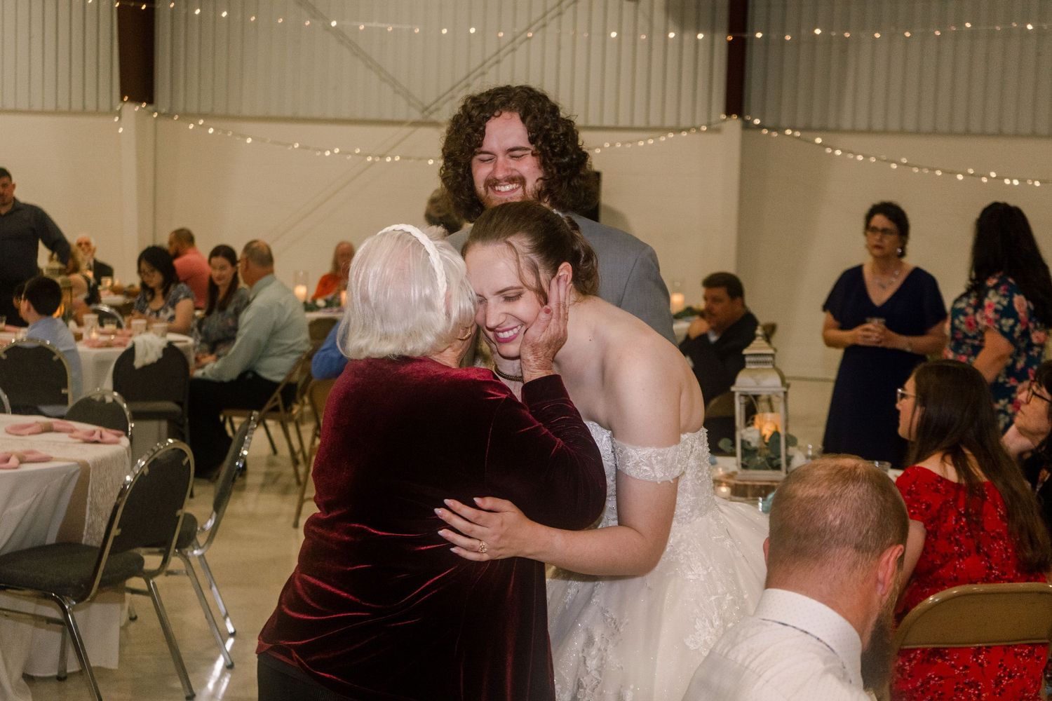 Wedding reception scene with guests embracing in a gathering space decorated with string lights.