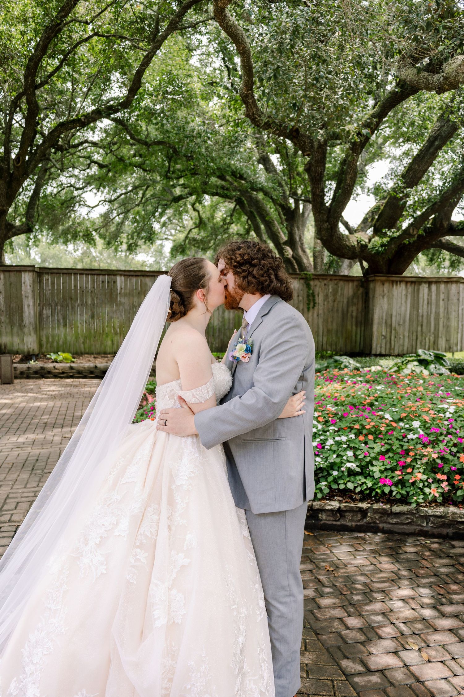 Couple sharing intimate moment under garden trees in wedding attire.