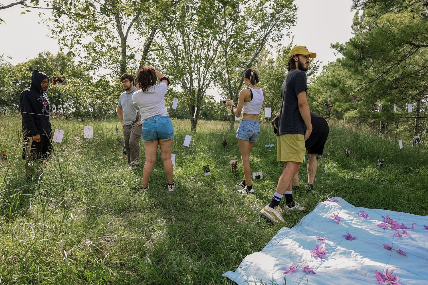 Group of young people walking through a lush green orchard with trees and white plant markers on a sunny day.