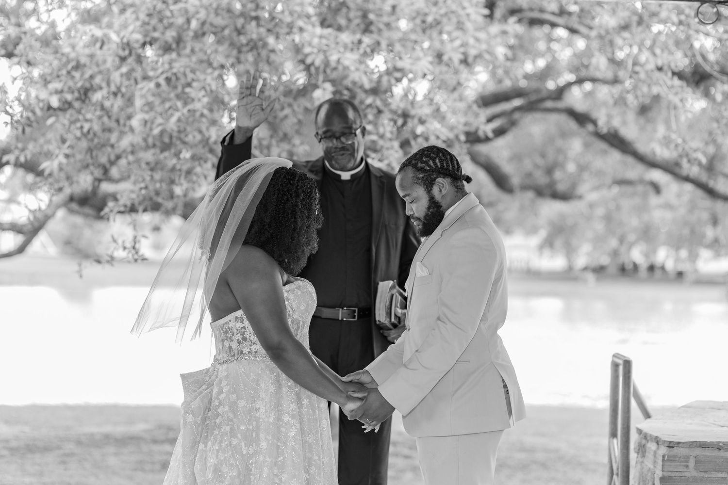 Wedding ceremony guests gather outdoors under trees on a sunny day.