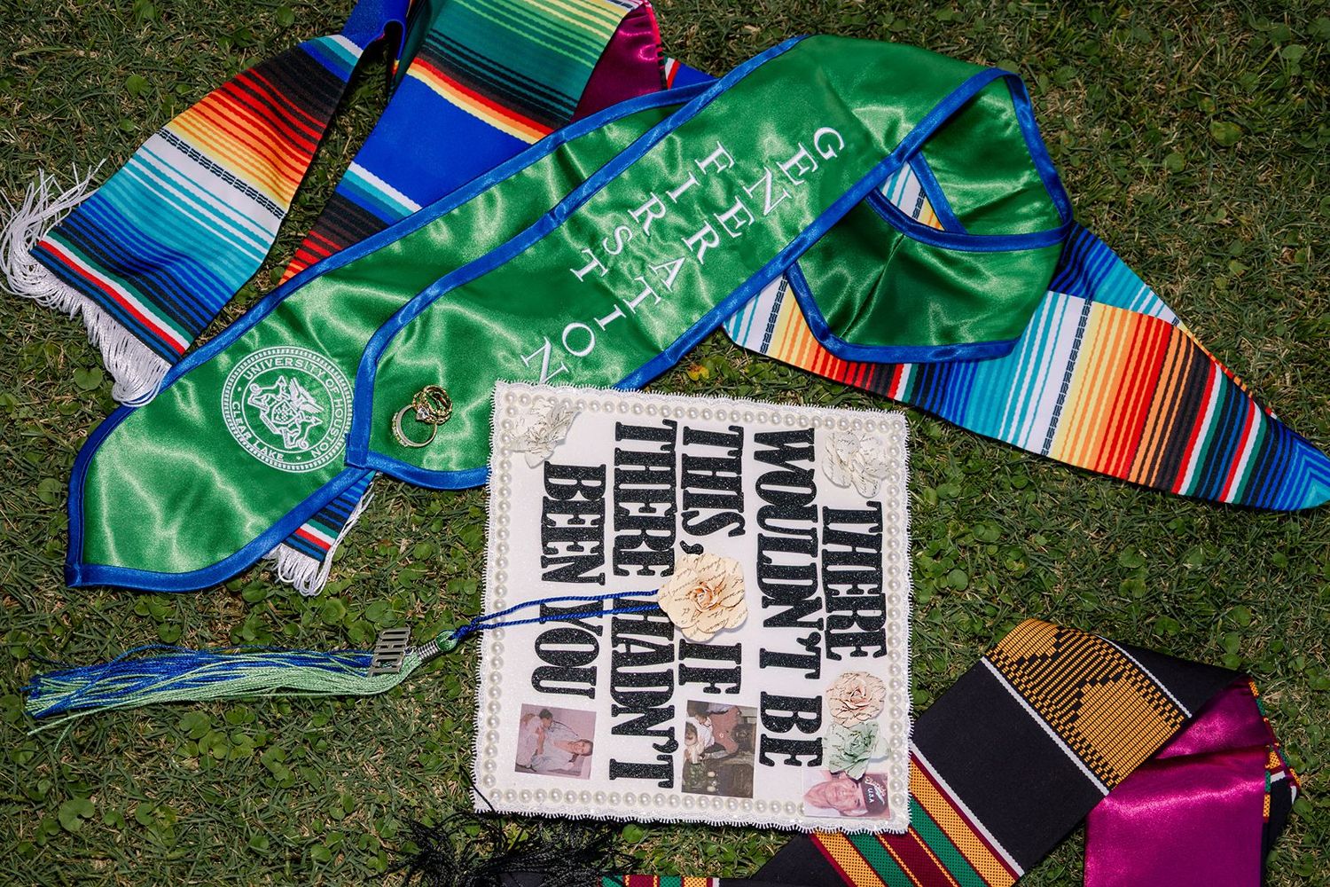 Graduation sashes, stoles, and a mortarboard cap with inspirational quote on grass.