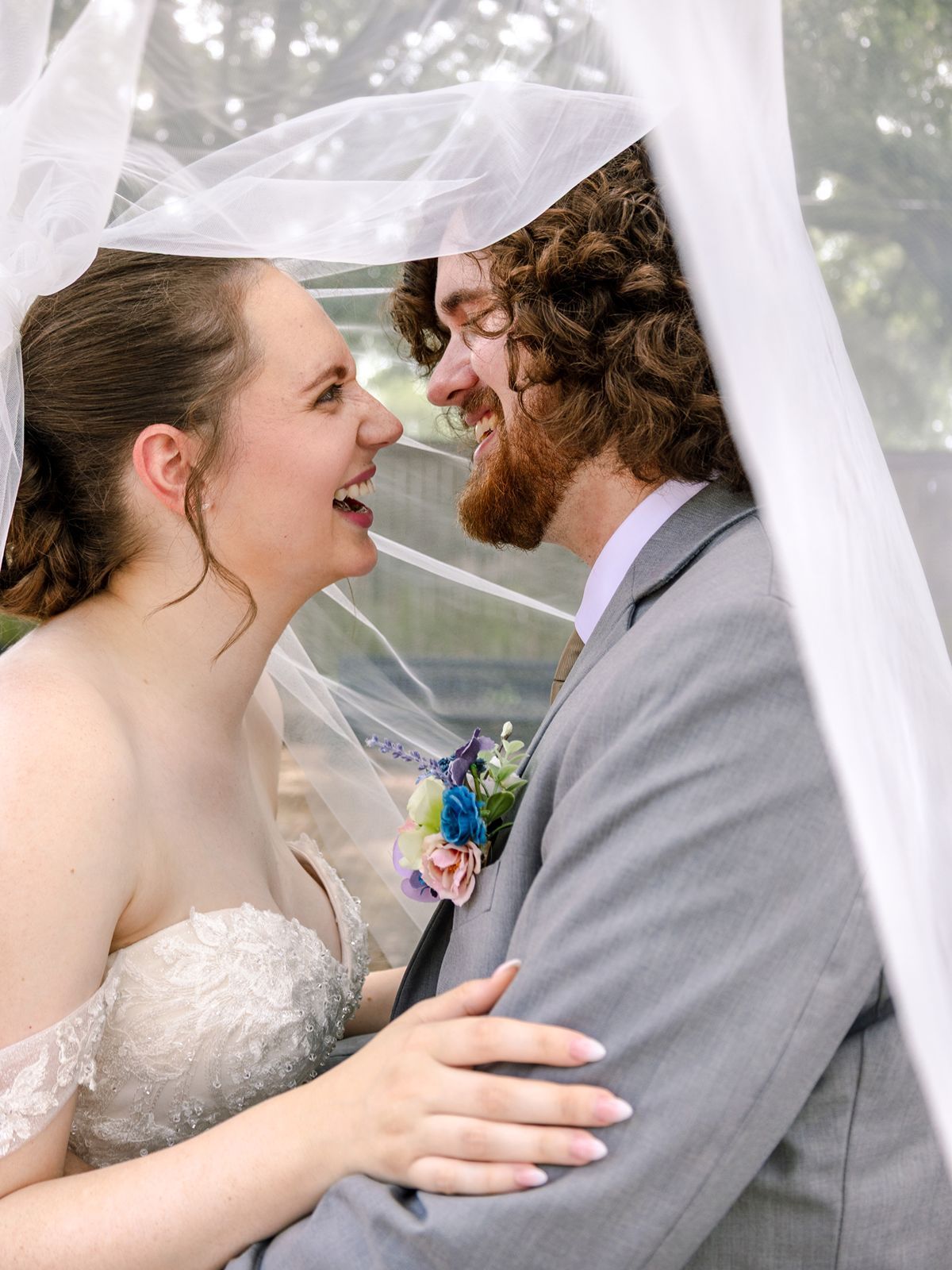 A bride and groom share a joyful moment together under a white veil during their wedding celebration.