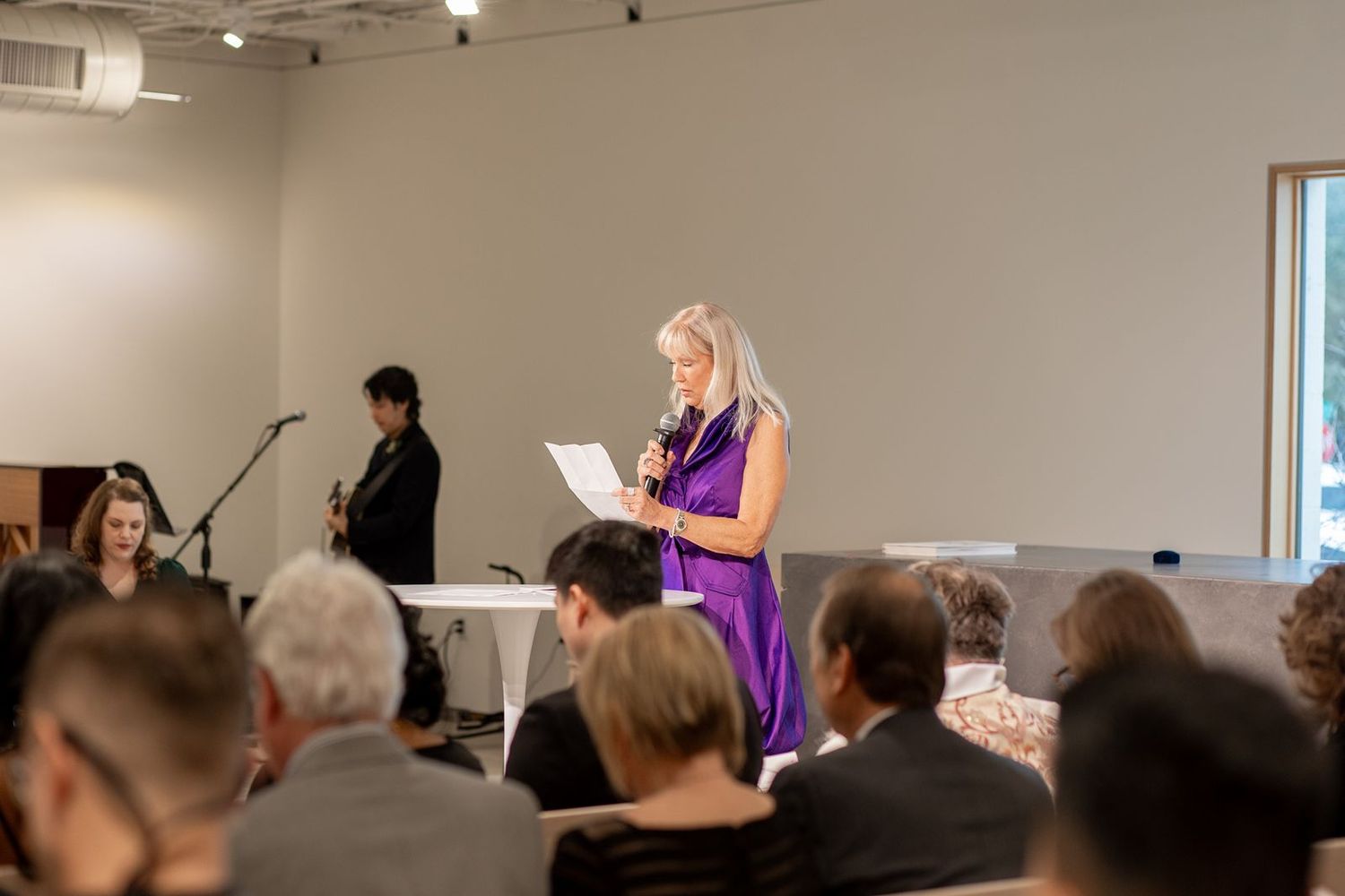 Wedding guests gather in an indoor venue with bright overhead lighting during a ceremony.