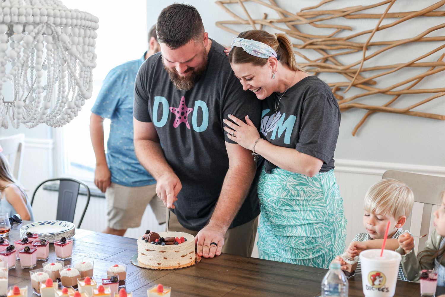 People gather around a dessert table with cupcakes and treats at a party celebration.