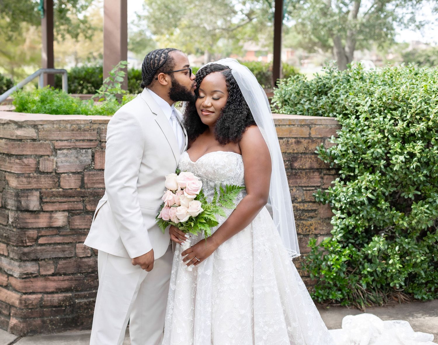 A bride and groom share tender moments in an outdoor garden setting with brick walls and lush greenery.