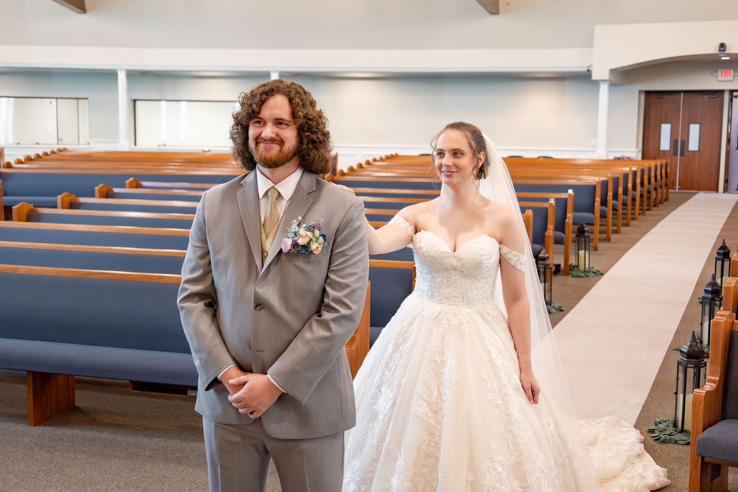 Wedding couple poses in a church sanctuary with exposed wooden beams and blue pew seating.