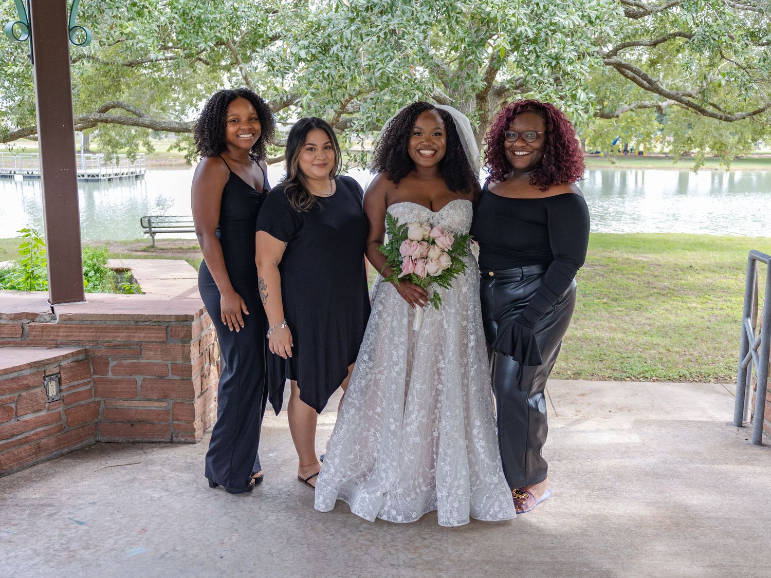 Wedding party in black and white dresses poses together under covered pavilion.