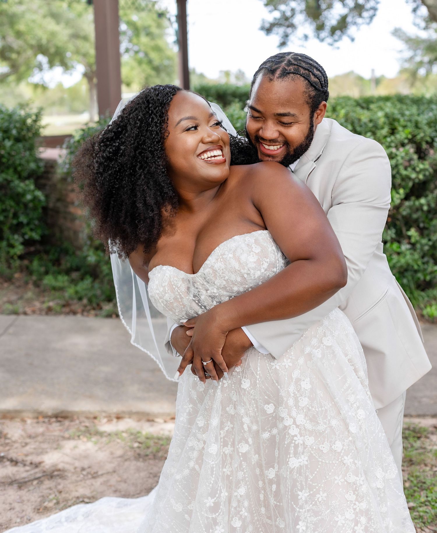 A couple laughs and embraces during their wedding photoshoot in a lush garden setting.