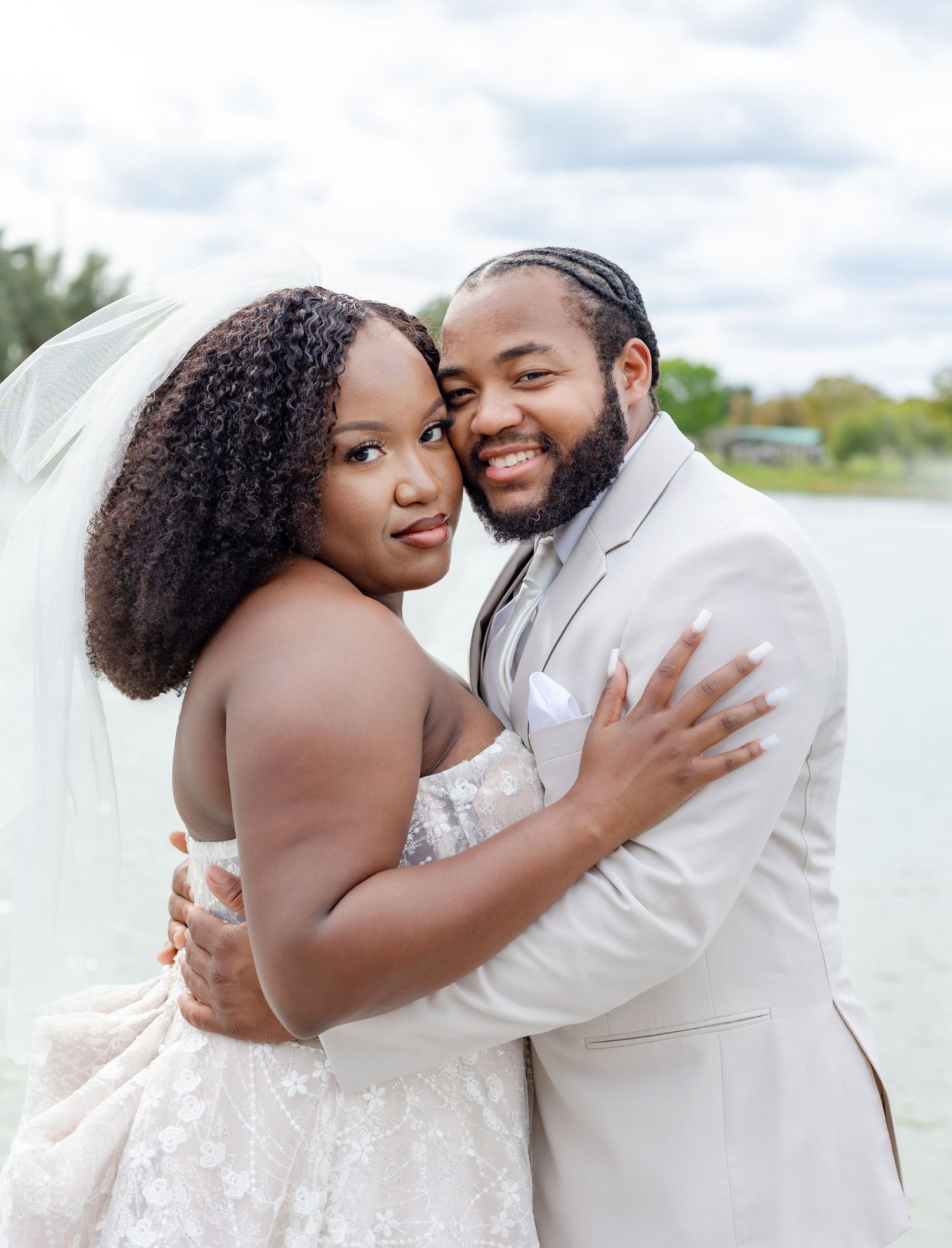 A joyful wedding portrait of newlyweds embracing by a waterfront setting.
