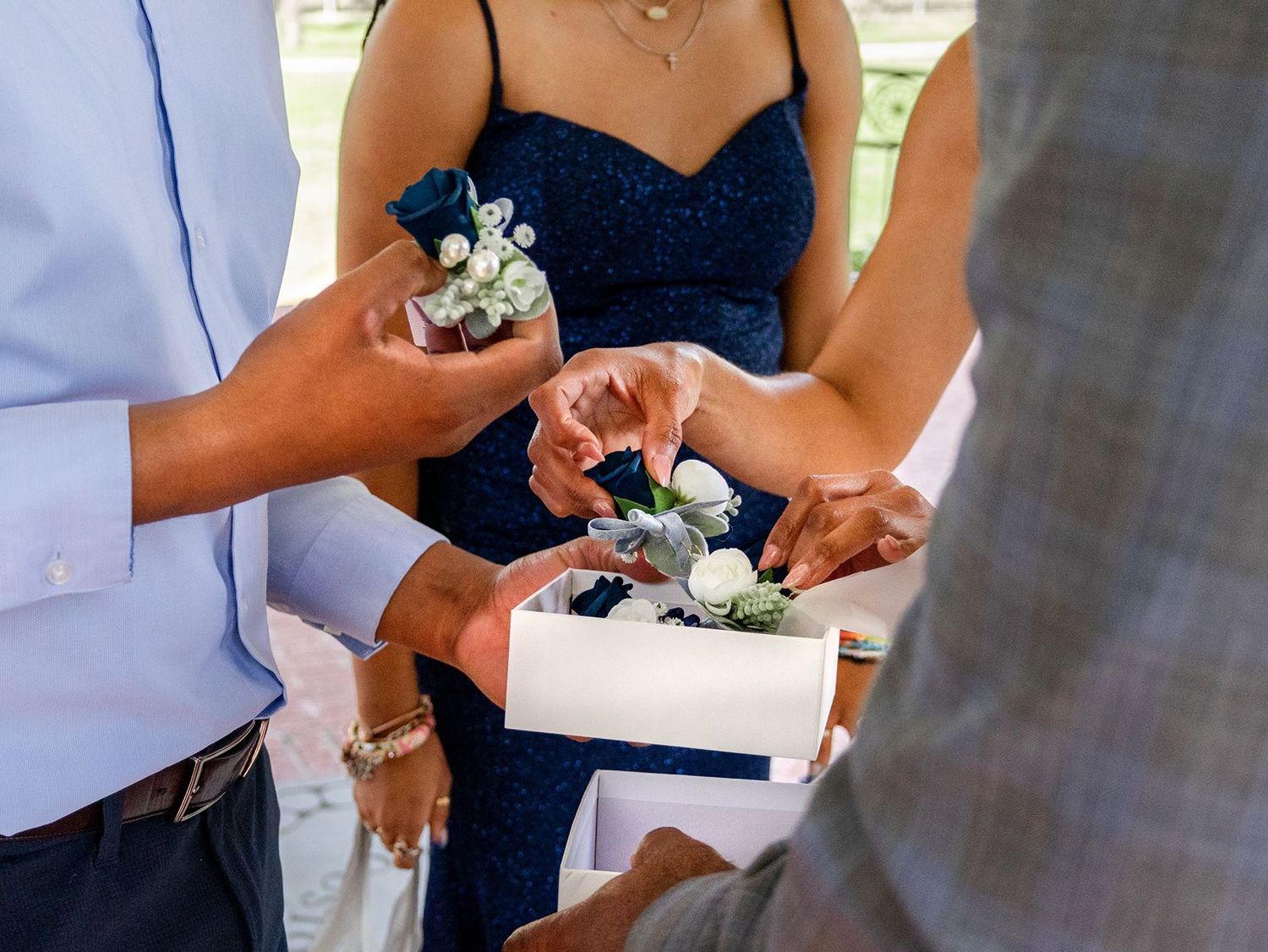 Hands pinning boutonniere flowers from white box at wedding ceremony.