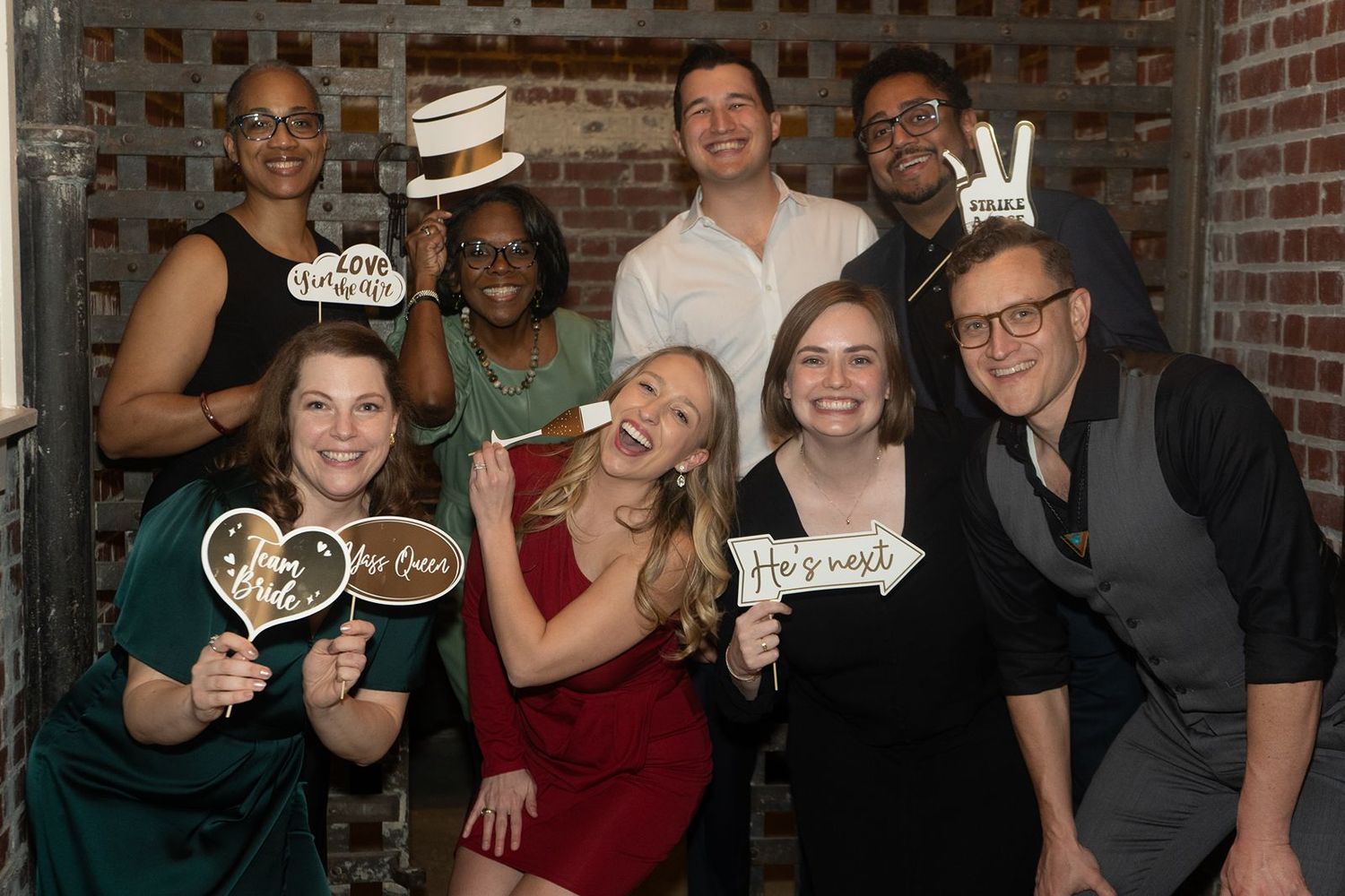 A group of people hold up wooden signs and decorations while posing together at a casual gathering.