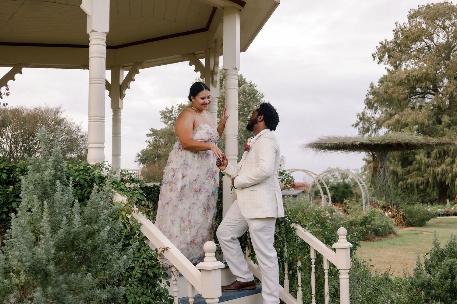 A couple shares a romantic moment on a white porch with elegant columns during their wedding celebration.