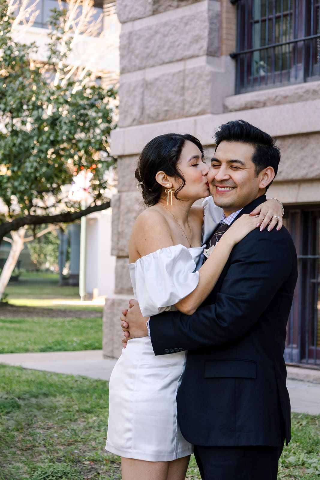 A romantic couple shares tender moments in formal attire outside a stone building.