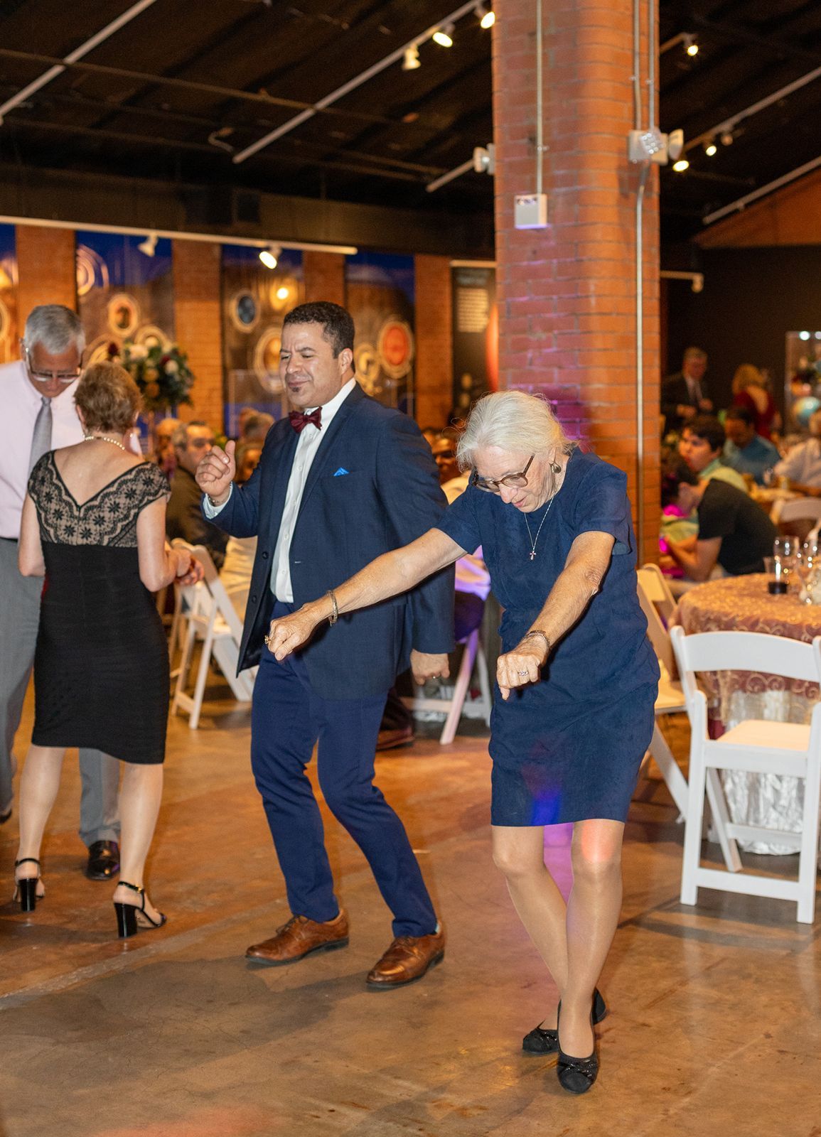 Dancers move energetically across a rustic brick-walled venue floor during a lively celebration.