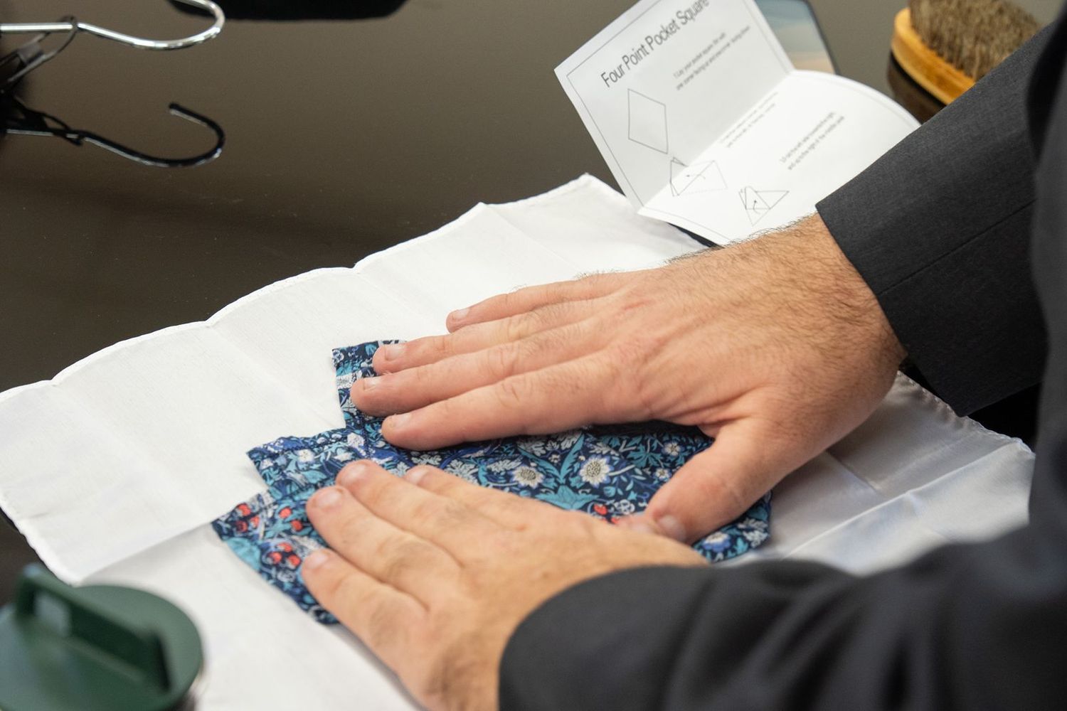 Close-up of hands smoothing a blue floral pocket square on white fabric for a wedding.