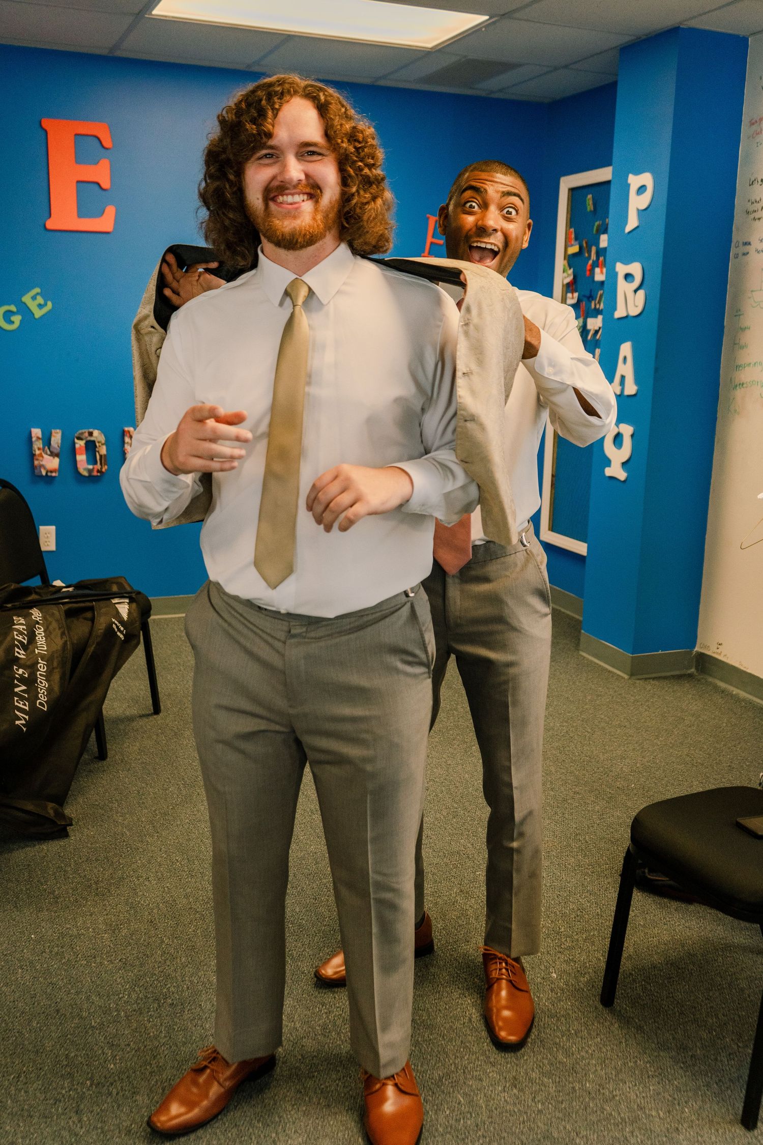 Groomsmen in grey suits and white shirts posing in a blue-walled room.
