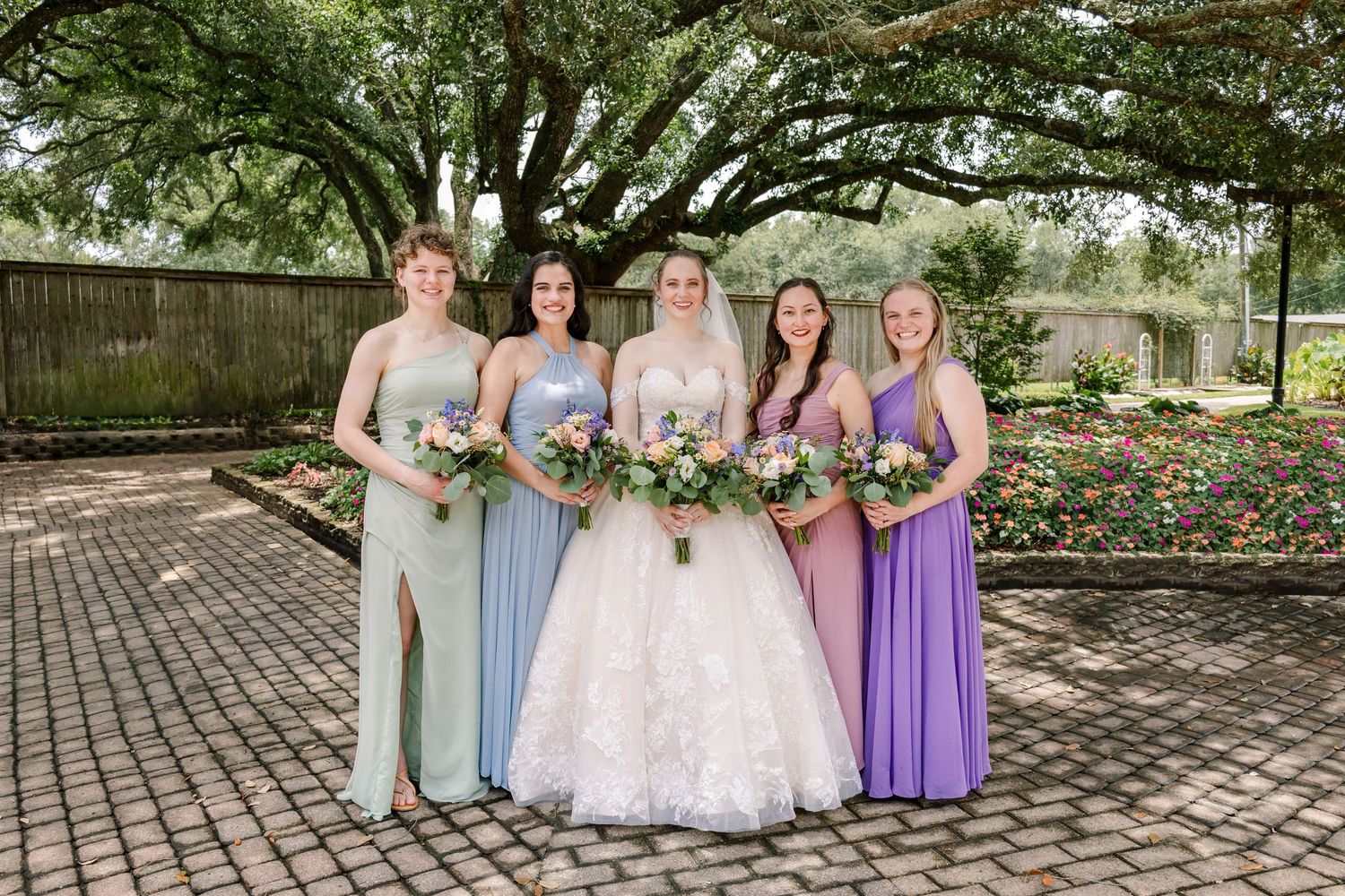 Bridal party in coordinated purple and blue dresses poses outdoors for formal photos.