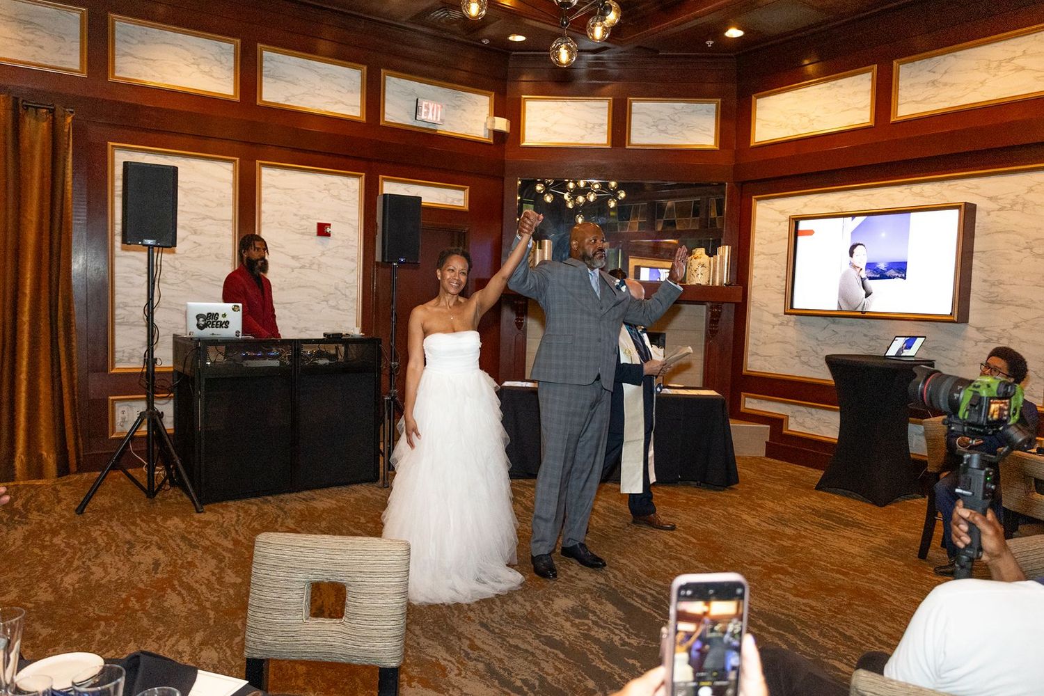 Bride and groom share first dance at elegant wedding reception with DJ and guests in warmly lit venue.