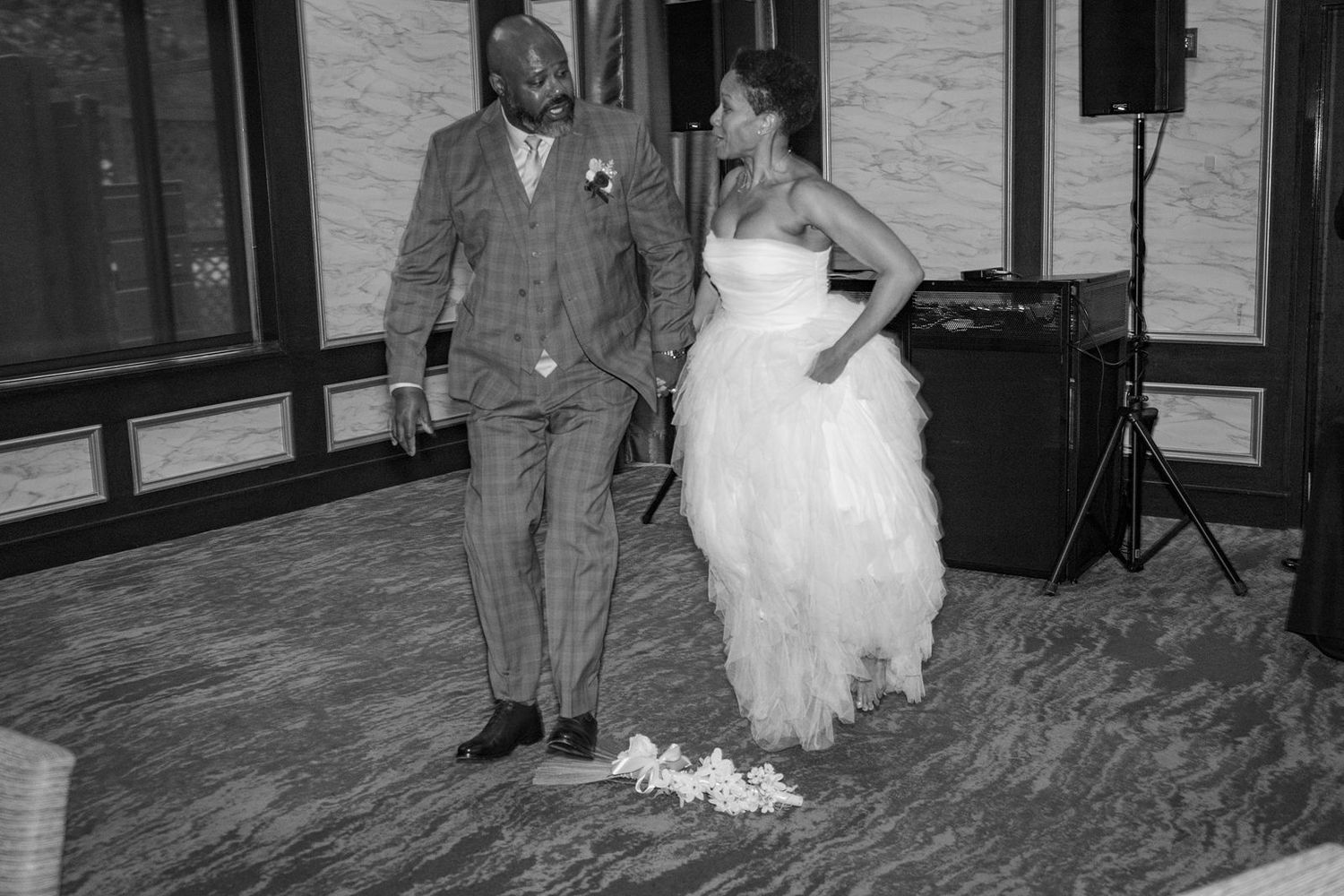 Black and white photo of bride and groom on dance floor with floral broom after jumping the broom ceremony.